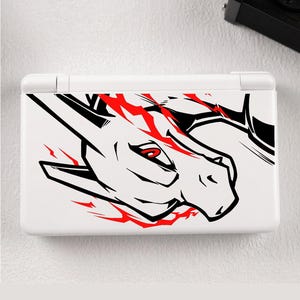 May include: A white handheld gaming console featuring a black and red graphic illustration of a dragon-like creature's head on the top cover. The design includes bold black outlines, sharp angular features, and vibrant red accents around the eye.