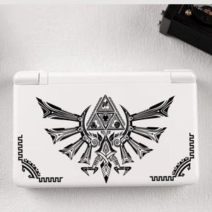 Peut inclure: Console de jeu portable blanche avec un motif graphique noir d'un blason stylisé avec un triangle au centre. La console a une conception à charnière et est posée sur un fond blanc.
