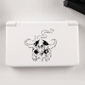 May include: A white handheld gaming console featuring a black ink-style graphic on the lid. The illustration depicts a stylised creature with flowing, smoke-like appendages, sharp claws, and a pointed head, centred within a solid black circle.