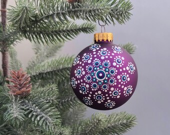 May include: Purple Christmas ornament with a white and blue mandala design. The ornament is hanging from a Christmas tree.