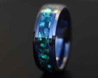 May include: A blue and silver ring with a green and blue opal inlay. The ring is a men's wedding band.