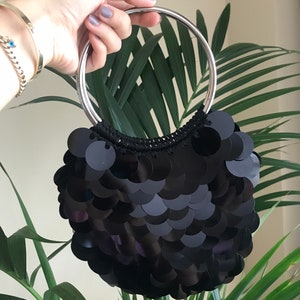 Può includere: Una borsa da sera nera con paillettes e un manico ad anello argentato.