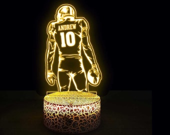 May include: A yellow 3D printed night light shaped like a football player. The player is wearing a jersey with the name "ANDREW" and the number "10" on the back. The night light is on a textured base.