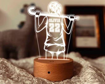 May include: A wooden base with a white silhouette of a person holding a hockey stick. The silhouette is wearing a jersey with the name "Olivia" and the number "22" on the back.