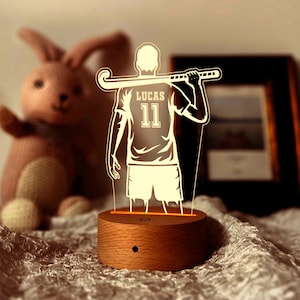 Puede incluir: Una base de madera con un diseño 3D iluminado de un jugador de hockey sosteniendo un palo. El jugador lleva una camiseta con el nombre "Lucas" y el número "11" en la espalda.