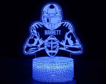 May include: Blue 3D printed night light featuring a football player in a helmet holding a football. The player's name "BARRETT" is printed on the jersey.