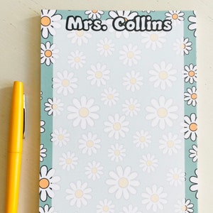 May include: A light blue notepad with a white daisy pattern and a black border. The notepad has the text "Mrs. Collins" at the top.