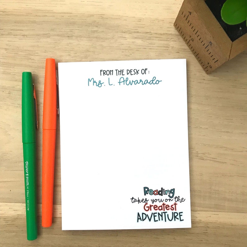Pu&ograve; includere: Blocco note bianco con testo blu e nero che dice "FROM THE DESK OF: Mrs. L. Alvarado". La parte inferiore del blocco note ha testo colorato che dice "Reading takes you on the Greatest ADVENTURE".