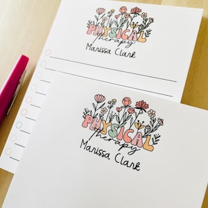 May include: Two white notepads with a floral design and the text "PHYSICAL therapy Marissa Clark". The notepads have a lined section for writing.