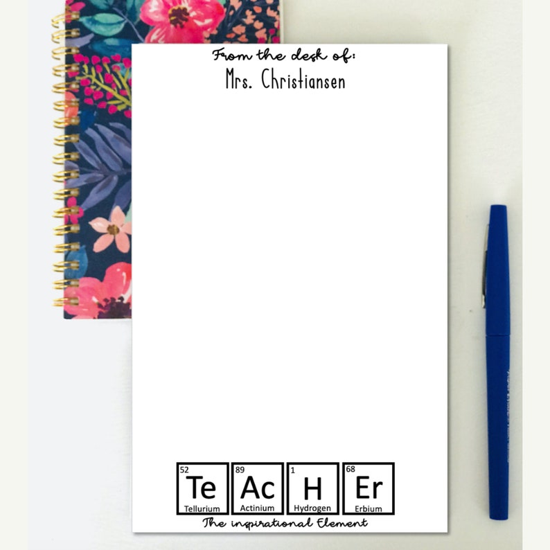 以下が含まれることがあります： 「From the desk of: Mrs. Christiansen」というテキストが上部に書かれた白いメモ帳。メモ帳の下部には、Te、Ac、H、Erの元素が強調表示された白黒の周期表のグラフィックがあります。「The inspirational element」というテキストがグラフィックの下にあります。