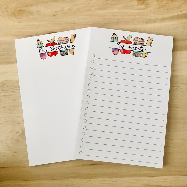 May include: Two white notepads with lined pages and a checklist. The top of each notepad has a colorful illustration of a red apple, a coffee cup, a pencil, and a ruler. The text "Mrs. Shelbourne" is on the left notepad and "Mrs. Arents" is on the right notepad.