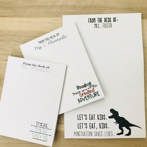 Pu&ograve; includere: Quattro blocchi note bianchi con testo nero. Il blocco note superiore dice "From the desk of: Mrs. Fulfer". Il secondo blocco note dice "From the desk of: Mrs. L. Alvarado". Il terzo blocco note dice "From the desk of: Mrs. Hernandez". Il quarto blocco note ha una silhouette nera di un dinosauro e dice "Let's eat kids. Let's eat, kids. Punctuation saves lives." Il blocco note ha anche una grafica colorata che dice "Reading takes you on the Greatest Adventure."