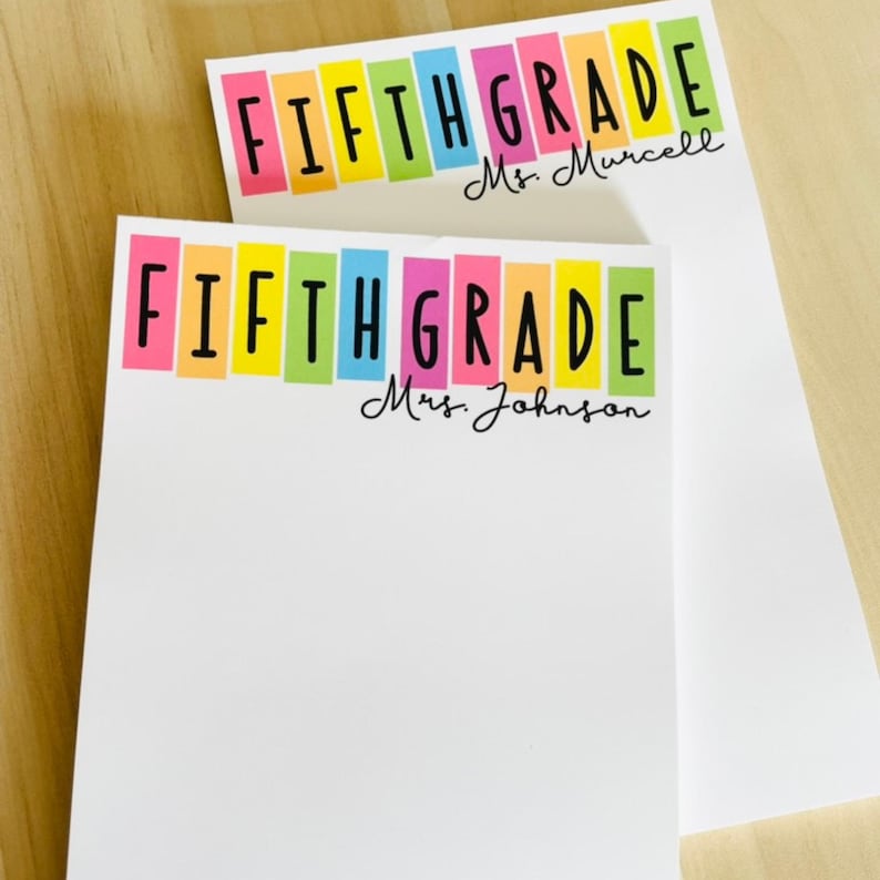 May include: Two white notepad sets with colorful stripes and the text "FIFTH GRADE" with the teacher's name below. The top notepad says "Mrs. Murcell" and the bottom notepad says "Mrs. Johnson".