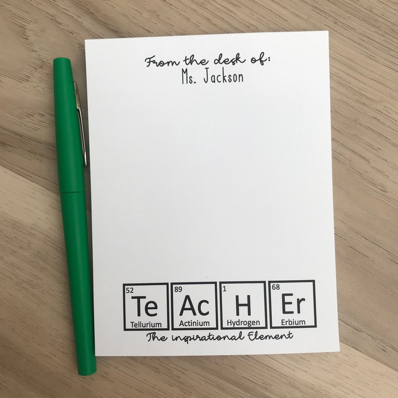 以下が含まれることがあります： 「From the desk of: Ms. Jackson」という黒い文字が書かれた白いメモ帳。テキストの下には、Te、Ac、H、Erの4つの化学元素の図があります。元素の下のテキストは「The inspirational Element.」です。