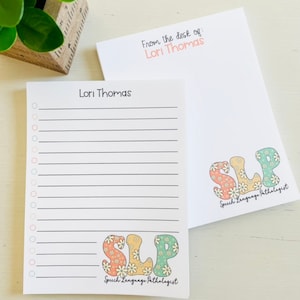 May include: A notepad with a floral design and the text "SLP Speech Language Pathologist" on the bottom. The notepad has a lined section and a blank section with the name "Lori Thomas" at the top.