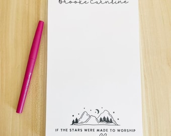 May include: White notepad with black text that reads "Brooke Carnline" at the top and "If the stars were made to worship so will I" at the bottom. A black and white illustration of mountains, stars, and a crescent moon is in the center of the notepad.
