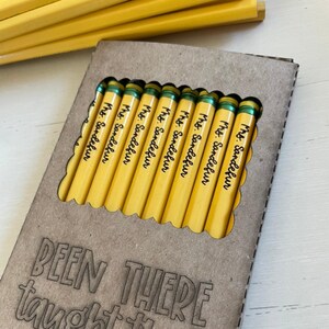 May include: A box of yellow pencils with green accents, each pencil is labeled "Mrs. Sandefur". The box is made of brown cardboard and has the text "BEEN THERE taught that" printed on the front.