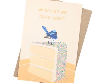 Peut inclure: Une carte de vœux avec un oiseau bleu perché sur un morceau de gâteau avec des pépites colorées. Le texte sur la carte dit "Wren can we have cake?"