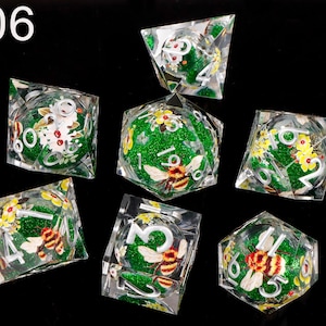 May include: Set of seven green and clear dice with a glitter finish. Each die features a bee and floral design. The dice are numbered 1 through 6.