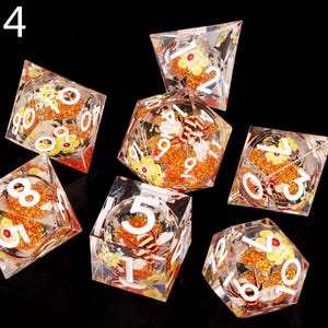 May include: Set of seven clear dice with orange and yellow glitter and floral designs. The dice are numbered 1 through 6 and have a bee design on the 6 side.