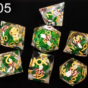 May include: Set of seven green and gold dice with a bee and flower design. The dice are numbered 1 through 6.