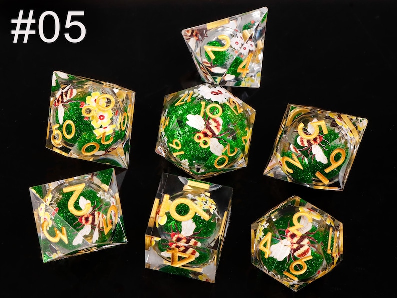 May include: Set of seven green and gold dice with a bee and flower design. The dice are numbered 1 through 6.