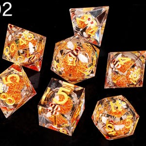 May include: Set of seven clear dice with gold numbers and bee and flower designs. The dice are filled with orange glitter.