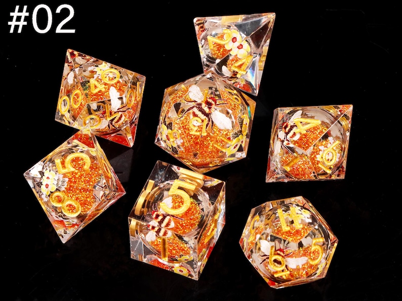 May include: Set of seven clear dice with gold numbers and bee and flower designs. The dice are filled with orange glitter.