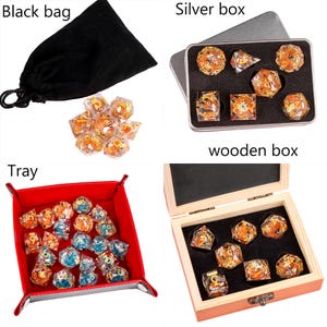 May include: A set of polyhedral dice with gold and orange accents, shown in a black velvet bag, a silver box, a wooden box, and a red felt tray. The dice are clear and have a variety of shapes.