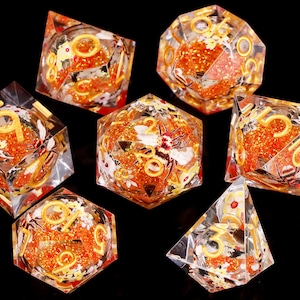 May include: Set of seven clear dice with orange glitter and gold accents. Each die has a different number from 1 to 7. The dice are decorated with white flowers and a bee.
