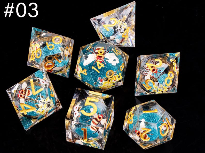 May include: Set of seven turquoise and gold dice with bee and flower designs. The dice are made of clear resin with a glittery finish. The numbers on the dice are in gold.
