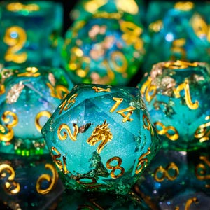May include: A set of teal blue dice with gold flecks and numbers. The dice are made of resin and have a sparkly finish. The dice are perfect for tabletop gaming.