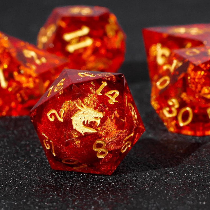May include: A set of red and gold dice with a dragon design. The dice are made of clear glass with gold flecks and have numbers and a dragon image on each side.
