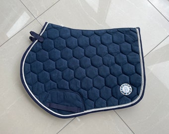 May include: A navy blue saddle pad with a white piping and a honeycomb quilted design. The saddle pad has a blue and white logo with the letter "B" in the center.