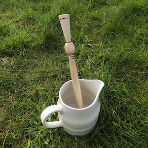 May include: A white ceramic jug with a wooden stirring stick inside. The jug is sitting on green grass.