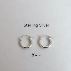 May include: A pair of small, circular sterling silver hoop earrings. The text "Sterling Silver" is printed above the hoops, and the text "10mm" is printed below them, indicating the diameter of the silver jewelry pieces.