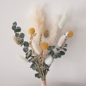 May include: A dried flower bouquet featuring pampas grass, eucalyptus, and yellow pom poms tied with twine.