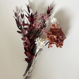 May include: A bouquet of dried flowers in shades of burgundy, pink, and white. The bouquet includes burgundy leaves, pink berries, and white flowers.