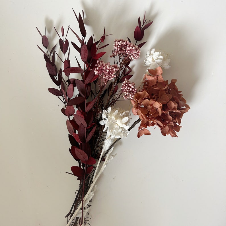 May include: A bouquet of dried flowers in shades of burgundy, pink, and white. The bouquet includes burgundy leaves, pink berries, and white flowers.