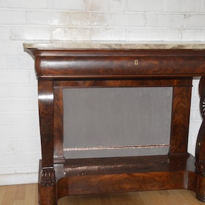 May include: A dark brown wooden console table featuring a rectangular marble top, a single drawer with a central keyhole, and curved legs that terminate in carved feet. The piece includes a lower shelf and a flat, solid back panel.