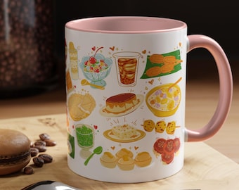May include: White ceramic mug with a pink interior and handle, decorated with colorful illustrations of various desserts. The mug is sitting on a wooden surface with a spoon and a macaron.