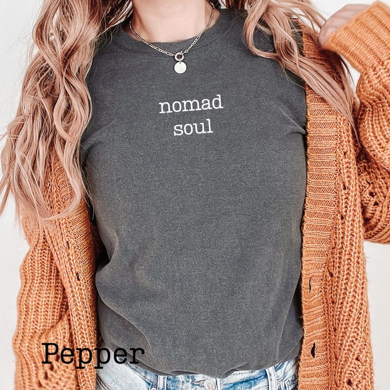 May include: A dark gray t-shirt with the words "nomad soul" in white. The shirt is paired with a rust-colored cardigan. The word "Pepper" is at the bottom of the image.