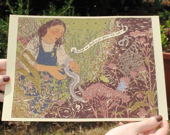 May include: A colorful art print featuring a woman in a blue apron interacting with a snake in a garden setting. The print includes the text "hold me fast and fear me not". The artwork has a vintage aesthetic.