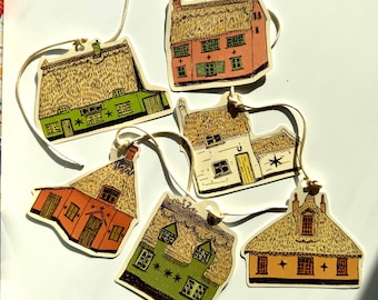 May include: A collection of six paper house ornaments with thatched roofs and various colors, including green, orange, and pink. Each house has a string for hanging. The ornaments are arranged on a white surface.