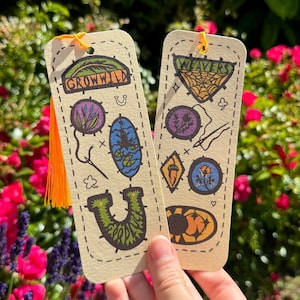 May include: Two colourful bookmarks with a whimsical design. The bookmark on the left has the text "Grow Wild" and features a variety of nature-inspired illustrations. The bookmark on the right has the text "Weavers" and features a spider web and other nature-inspired illustrations.