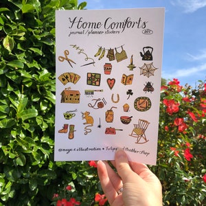 Puede incluir: Una hoja de pegatinas con ilustraciones de objetos hogare&ntilde;os acogedores, que incluyen una tetera, una mecedora, una casa, una herradura, una telara&ntilde;a, una abeja, un rat&oacute;n, una taza de t&eacute;, una vela, un libro, un coraz&oacute;n, un tr&eacute;bol de cuatro hojas, un par de calcetines, un su&eacute;ter de punto, un par de tijeras, una aguja e hilo, una colcha, una carta de juego, una sart&eacute;n, un taz&oacute;n, un muffin, un frasco y una escoba. La hoja se titula "Home Comforts Journal/Planner Stickers 001" e incluye el nombre de usuario de las redes sociales "@maya.c.illustration + Tulips + heather-shop".
