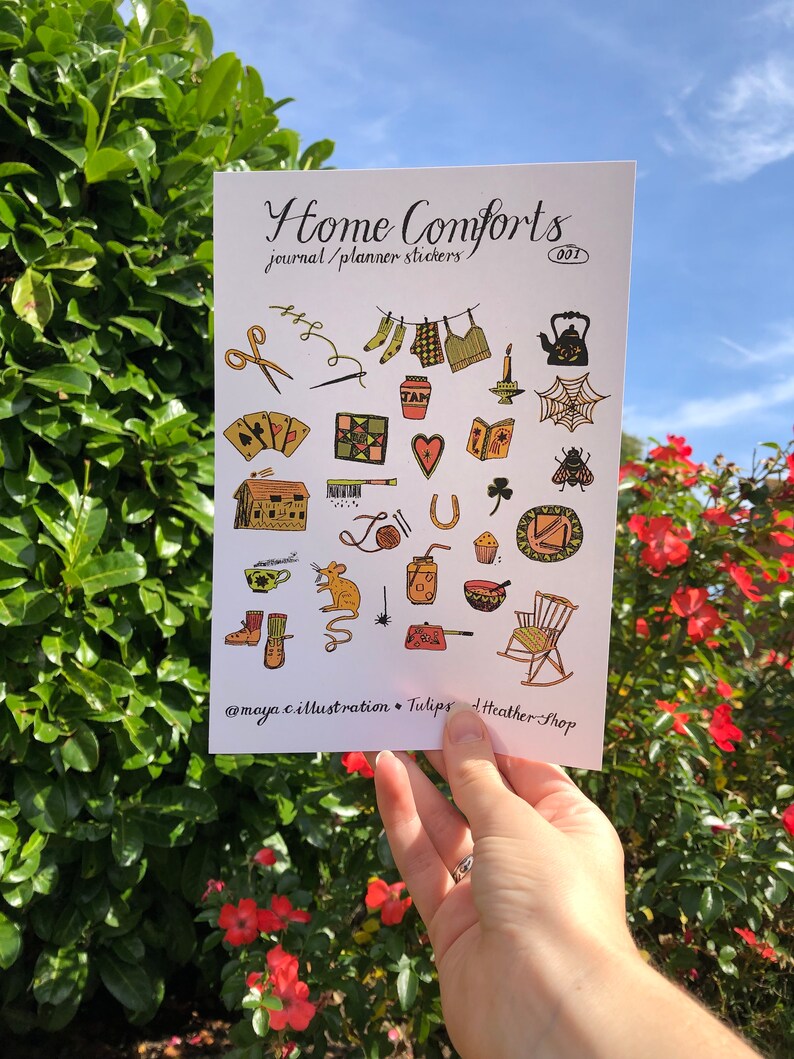 Puede incluir: Una hoja de pegatinas con ilustraciones de objetos hogare&ntilde;os acogedores, que incluyen una tetera, una mecedora, una casa, una herradura, una telara&ntilde;a, una abeja, un rat&oacute;n, una taza de t&eacute;, una vela, un libro, un coraz&oacute;n, un tr&eacute;bol de cuatro hojas, un par de calcetines, un su&eacute;ter de punto, un par de tijeras, una aguja e hilo, una colcha, una carta de juego, una sart&eacute;n, un taz&oacute;n, un muffin, un frasco y una escoba. La hoja se titula "Home Comforts Journal/Planner Stickers 001" e incluye el nombre de usuario de las redes sociales "@maya.c.illustration + Tulips + heather-shop".