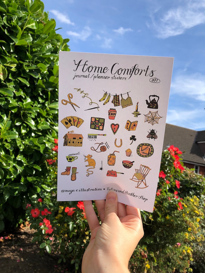 Puede incluir: Una hoja de pegatinas coloridas con ilustraciones de objetos hogare&ntilde;os como una tetera, una mecedora, una casa y una bola de lana. La hoja se titula "Home Comforts Journal/Planner Stickers 001" e incluye el nombre de usuario de las redes sociales @maya.c.illustration.