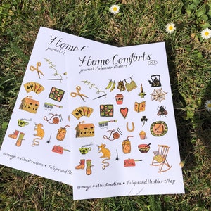 Puede incluir: Dos hojas de pegatinas con fondo blanco e ilustraciones coloridas. Las pegatinas son para diarios y planificadores. El texto en las pegatinas dice "Home Comforts" y "journal/planner stickers".