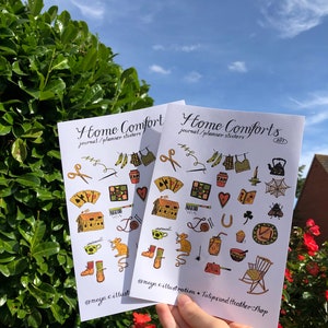 Puede incluir: Dos hojas de pegatinas con un tema hogare&ntilde;o. Las pegatinas presentan ilustraciones de una casa, una tetera, una mecedora, una telara&ntilde;a, un rat&oacute;n, una herradura, una taza de t&eacute;, una bota, una bola de lana, un coraz&oacute;n, un tr&eacute;bol, una abeja, una aguja de coser, un par de tijeras, un libro, una llave, un par de calcetines, una colcha, un frasco, un cupcake, una olla, una vela y una regadera. El texto en las pegatinas dice "Home Comforts journal/planner stickers 001" y "@maya.c.illust  TulipsandHeatherShop".